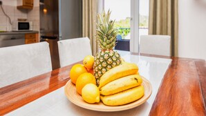 Ein Esstisch mit einer Fruchtschale, darunter Bananen, Zitronen und eine Ananas, sowie eine Mikrowelle im Hintergrund.
