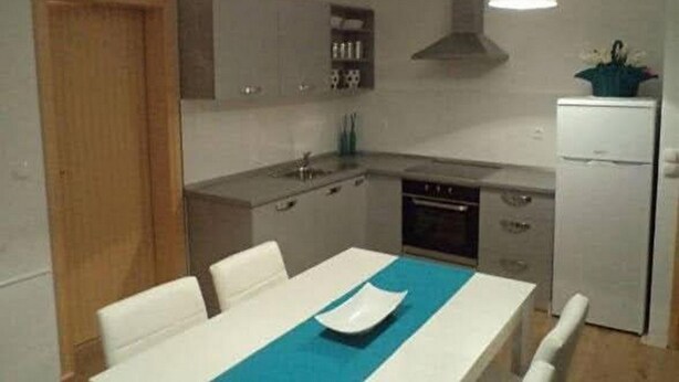 Eine kleine Küche mit Esstisch, weißen Schränken, einem Backofen und einem Kühlschrank.