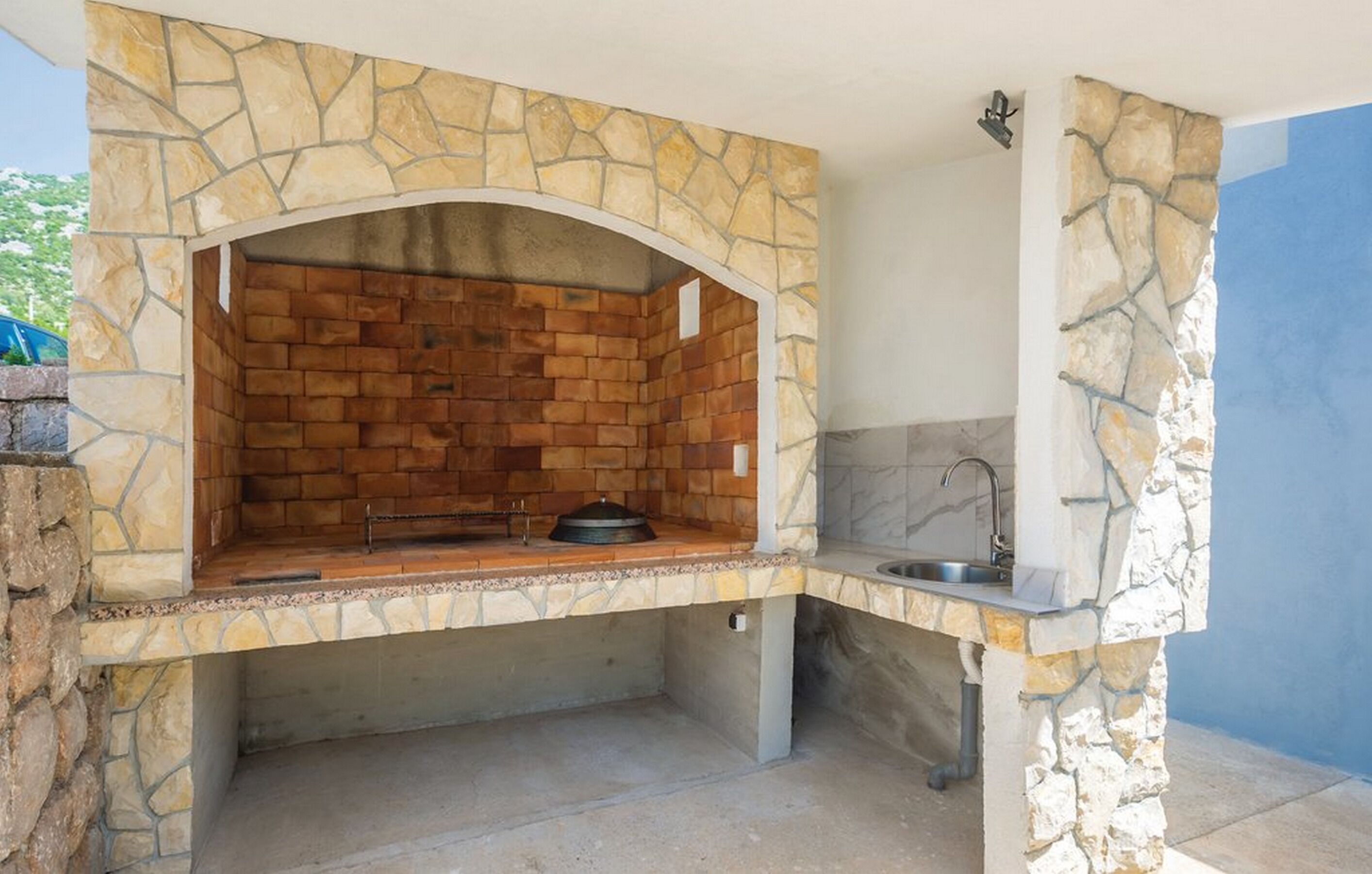 An outdoor kitchen with a stone arch structure, a sink, and a grill.