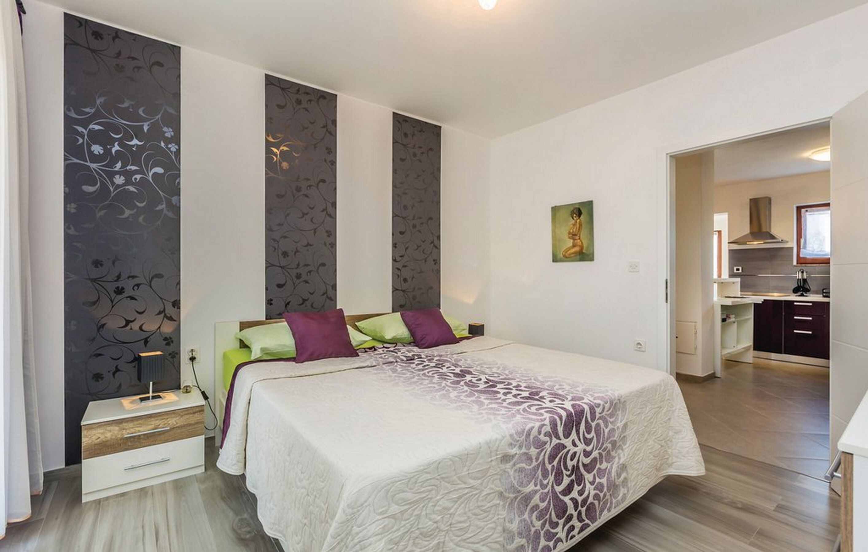 Ein Schlafzimmer mit Bett, Nachttisch und Blick zur Küche.