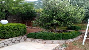 Jardim com paisagismo, parede de pedra, uma árvore e um objeto esférico branco.