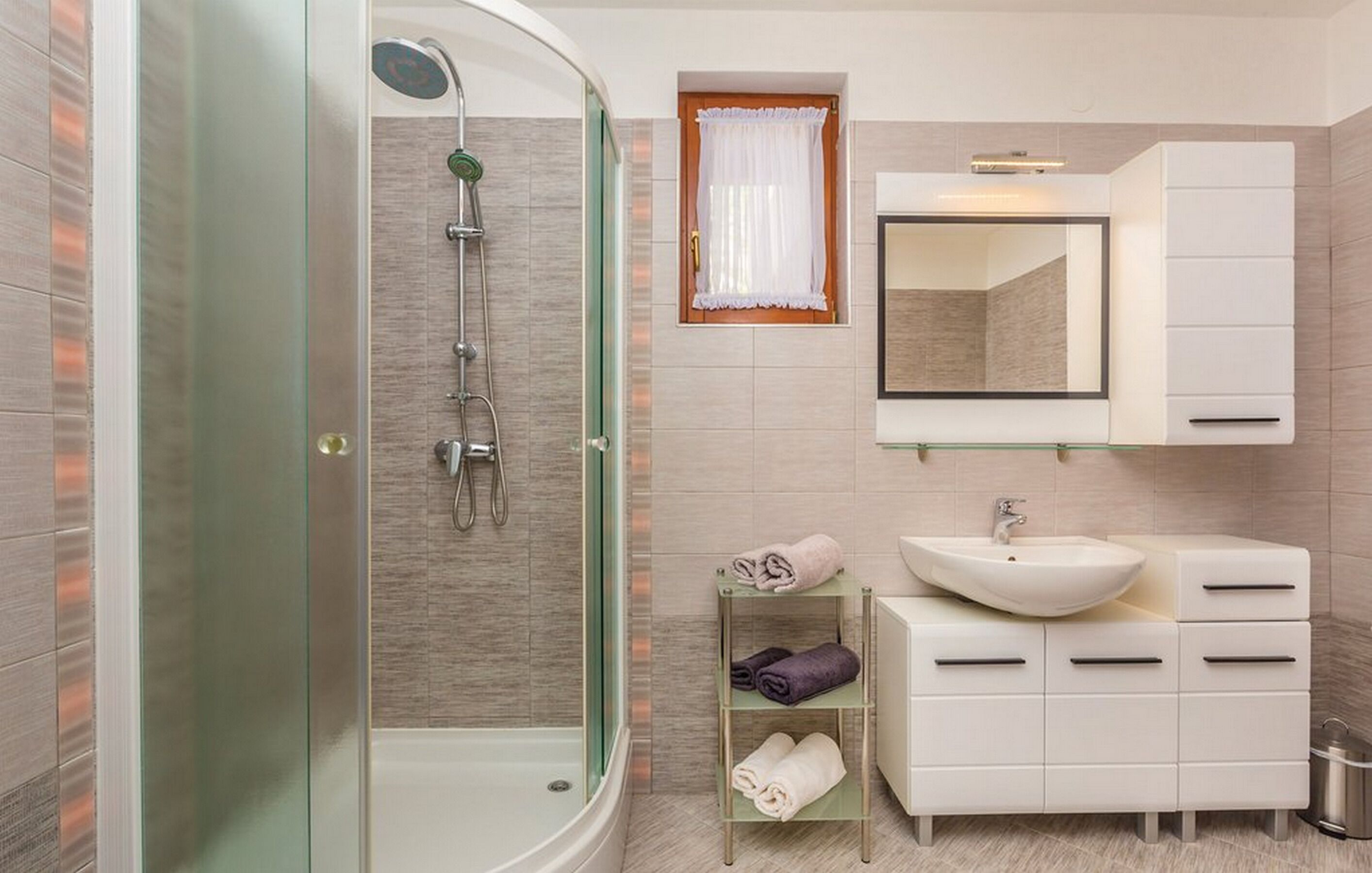 A modern bathroom with a glass-enclosed shower, a white sink, and a vanity with drawers.