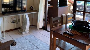 Un comedor con mesa y sillas de madera, un televisor sobre un soporte y una pequeña estatua en la pared.