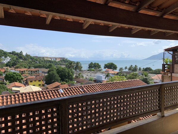 A balcony with a view of a coastal town, featuring terracotta rooftops and a wooden railing. - Beach house with ocean view and mountains for 8 people North Coast Sao Paulo (SAO SEBASTIAO)