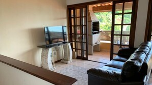 Una sala de estar con un sofá de cuero negro, un televisor de pantalla plana sobre un mueble bajo y una parrilla al otro lado de una puerta corrediza de vidrio.