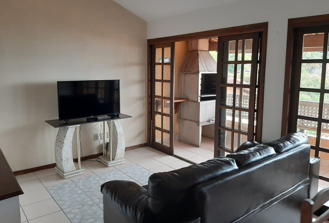 A living room with a black leather sofa, a television on a white pedestal, and a sliding glass door leading to an outdoor area.