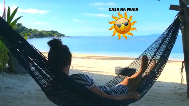 Una hamaca en una playa arenosa con vistas despejadas al mar y un paisaje tropical de fondo.