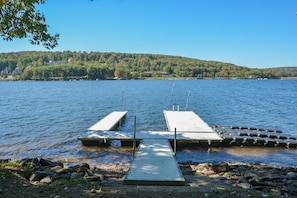 A lake with two wooden docks extending into the water, surrounded by a rocky shoreline and a forested hill in the background.