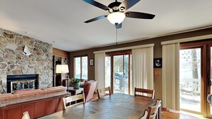 A spacious dining area with a stone fireplace, a ceiling fan, and a view of the outdoors through large sliding glass doors. - Blue Heron by Taylor Made Deep Creek (McHenry)