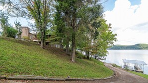 A lakeside property with a grassy slope, a wooden deck, and a small building. - Lake front with private dock & boat ramp (Waverly)