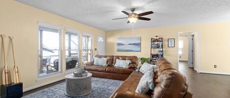 A spacious living room with a large brown leather sofa, a round coffee table, and a ceiling fan.
