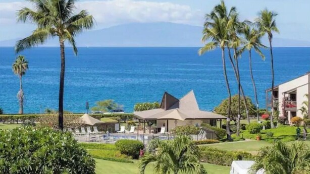 A resort with a pool area, palm trees, and a view of the ocean.