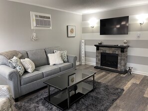 A modern living room with a grey sofa, a black coffee table, a fireplace, and a flat-screen TV.