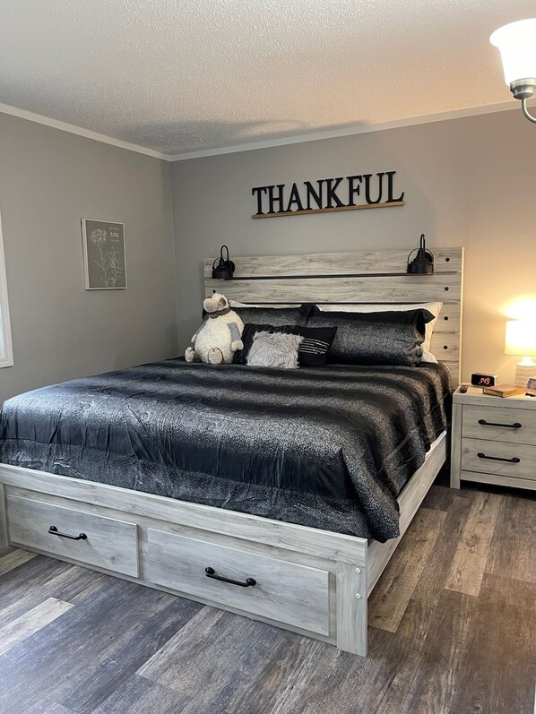 A bedroom with a bed, a nightstand, a wall-mounted shelf, and a 'THANKFUL' sign.