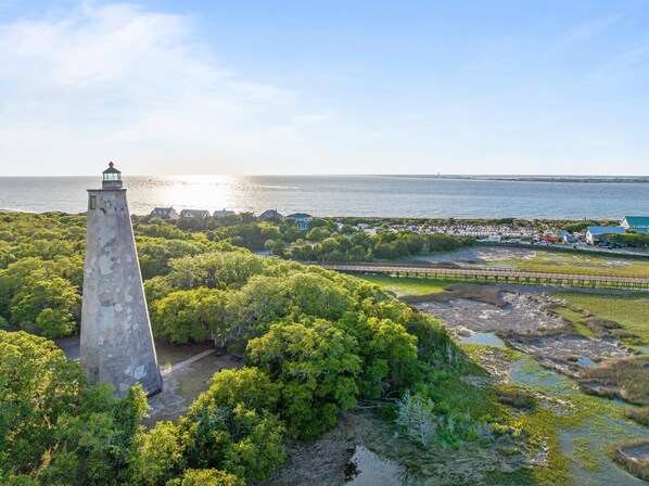 Een kustgebied met een vuurtoren, weelderige begroeiing en een strand met een steiger.