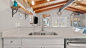 A kitchen with a granite countertop, stainless steel sink, and white cabinetry. - Seaside Serenity (Panama City Beach)