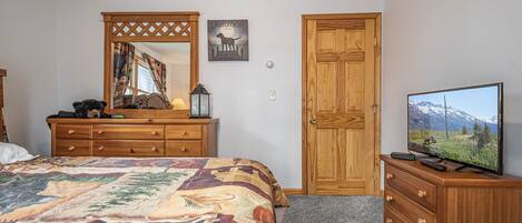 A bedroom with a bed, dresser, mirror, and a television on a stand.