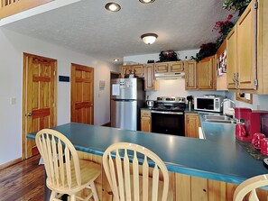 A kitchen with wooden cabinets, a stainless steel refrigerator, a stove, and a microwave. There are two wooden chairs at the kitchen island. - Black Bear Retreat by Taylor Made Deep Creek (McHenry)