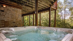 A hot tub with stone walls and wooden beams, surrounded by trees.