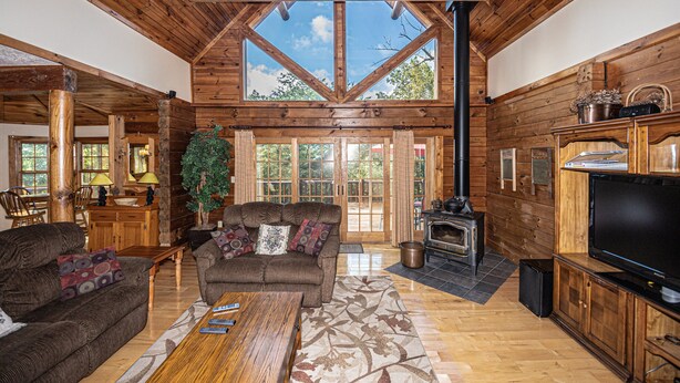 A log cabin interior with a large wooden ceiling, a fireplace, a television, and a dining area.
