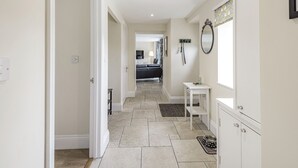 A hallway with a tiled floor leading to a bedroom with a bed and a TV. There is a small white table with a mirror and a cabinet. - Hebe (Dorchester)