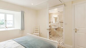 A bedroom with a bed, a window, a chair, and a bathroom visible through an open door. - Hebe (Dorchester)
