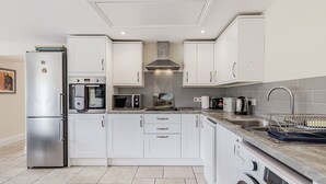 A modern kitchen with white cabinets, stainless steel appliances, a built-in oven, microwave, and dishwasher. - Hebe (Dorchester)