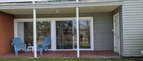 A covered patio with two blue chairs and a table, a sliding glass door, and a brick floor.