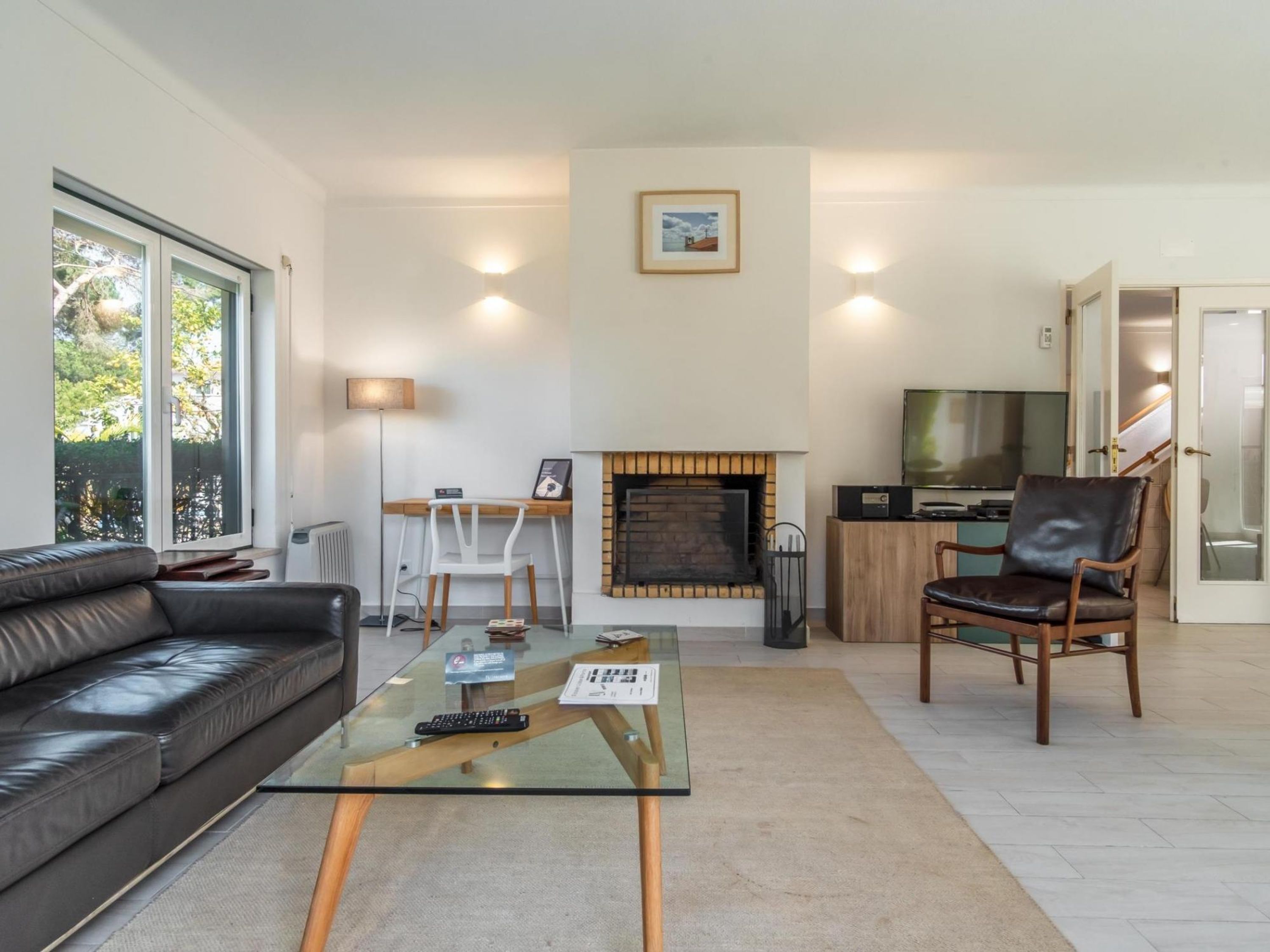 A modern living room with a glass coffee table, leather sofa, and a fireplace.