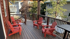 Eine Holzterrasse mit roten Adirondack-Stühlen und einem Tisch, umgeben von einem Metallgeländer.