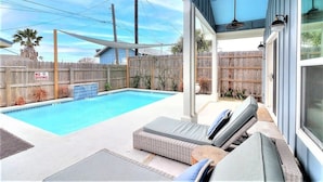A backyard with a swimming pool, lounge chairs, and a wooden fence.