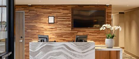 A modern reception area with a marble counter, wooden panel wall, and a large flat-screen TV.