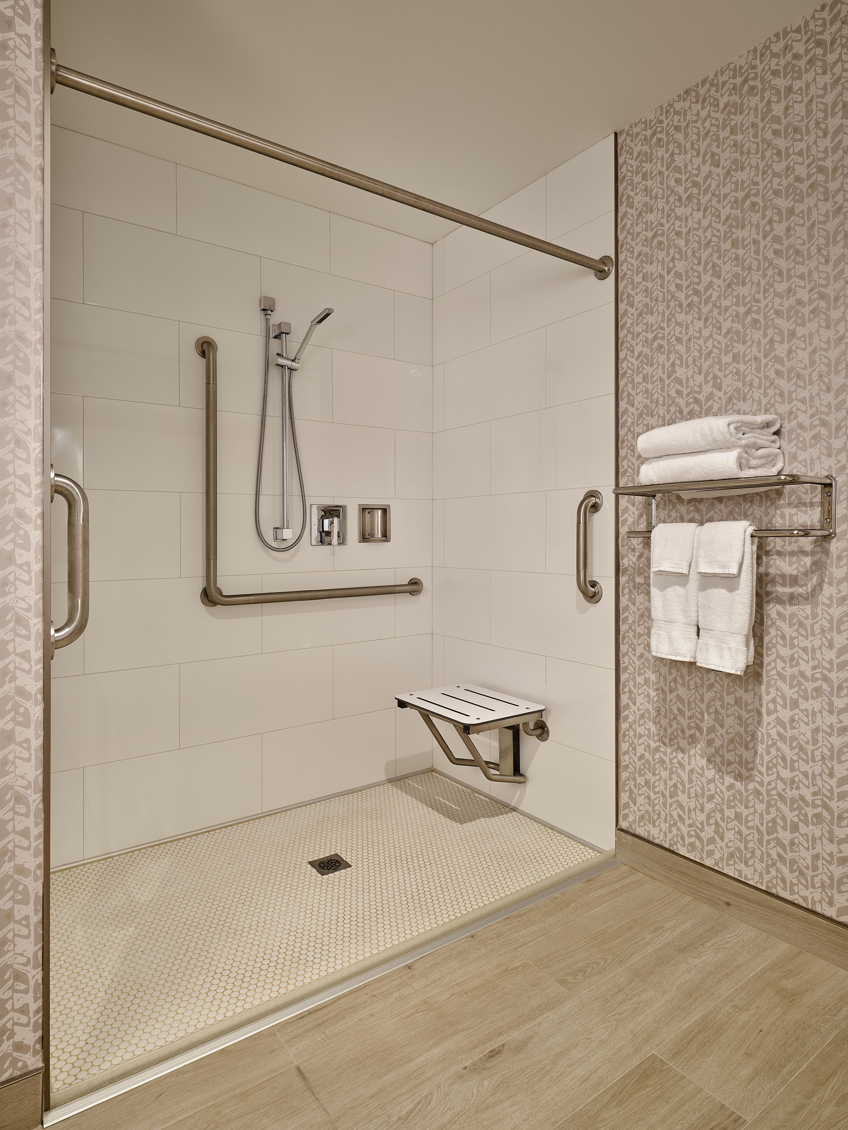 A modern bathroom with a walk-in shower, grab bars, a towel rack, and a patterned wall.