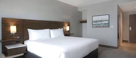 A modern hotel room with a large bed, two bedside tables with lamps, a framed picture on the wall, and a wooden door.