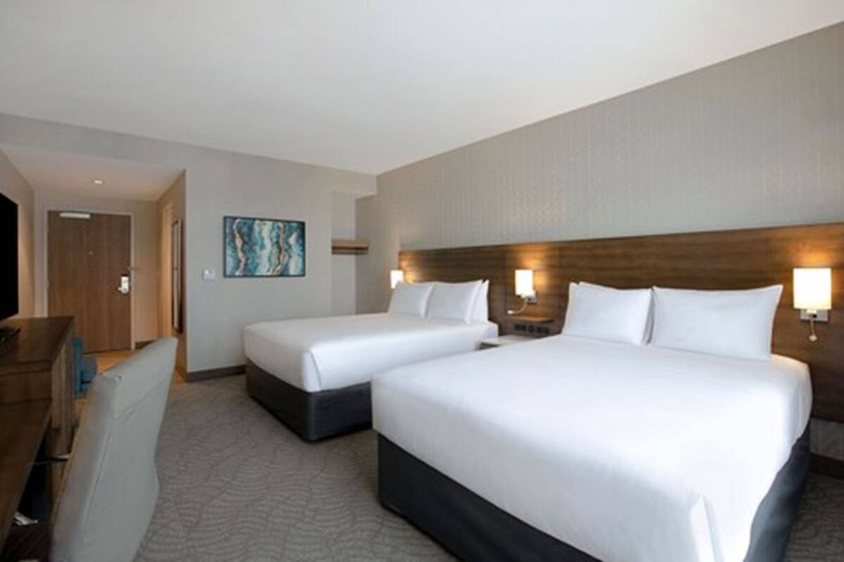 A hotel room with two beds, a desk, and a painting on the wall.