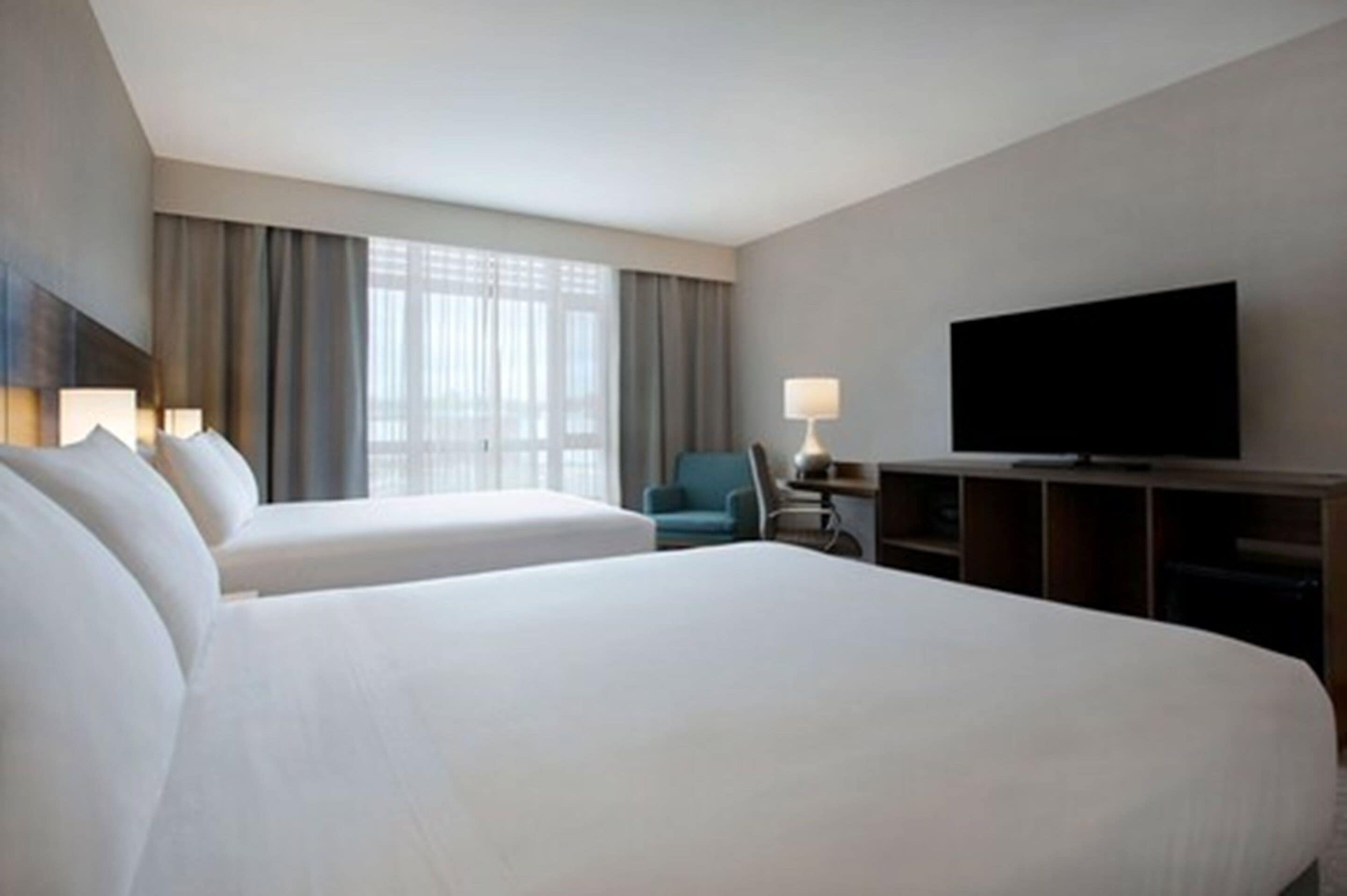 A hotel room with two beds, a television, a desk with a lamp, and a chair.