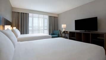 A hotel room with two beds, a television, a desk with a lamp, and a chair.