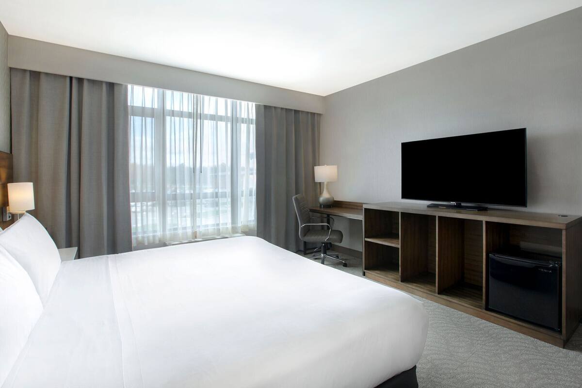 A hotel room with a large bed, a desk with a television, a chair, and a lamp.