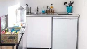 A compact kitchen with a microwave, a small sink, and a dishwasher. There is a countertop with various kitchen items and a blue container holding utensils. - "AU VINCI BLEU" Cosy - Downtown Amboise (Amboise)