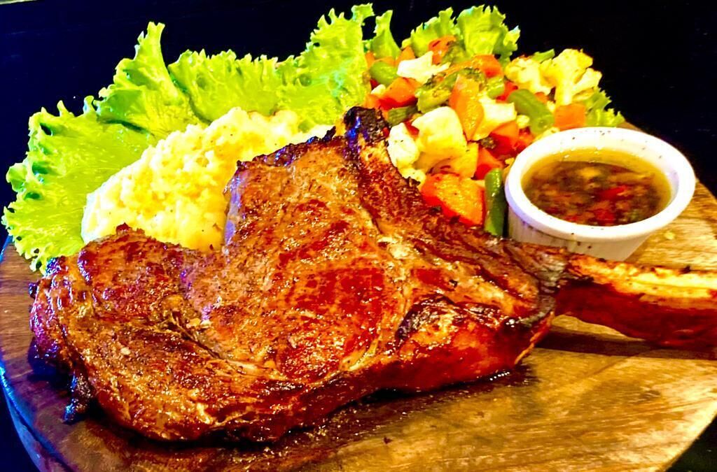Un plato con un filete a la parrilla, puré de papas, una ensalada pequeña y un recipiente con salsa.