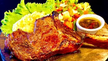 Un plato con un filete a la parrilla, puré de papas, una ensalada pequeña y un recipiente con salsa.