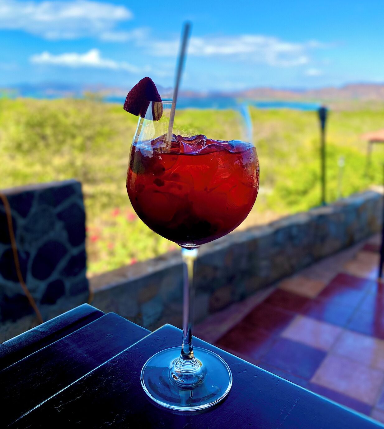Ein Glas rotes Getränk mit Trinkhalm und einer Kirsche auf einem Tisch, im Hintergrund eine schöne Aussicht.
