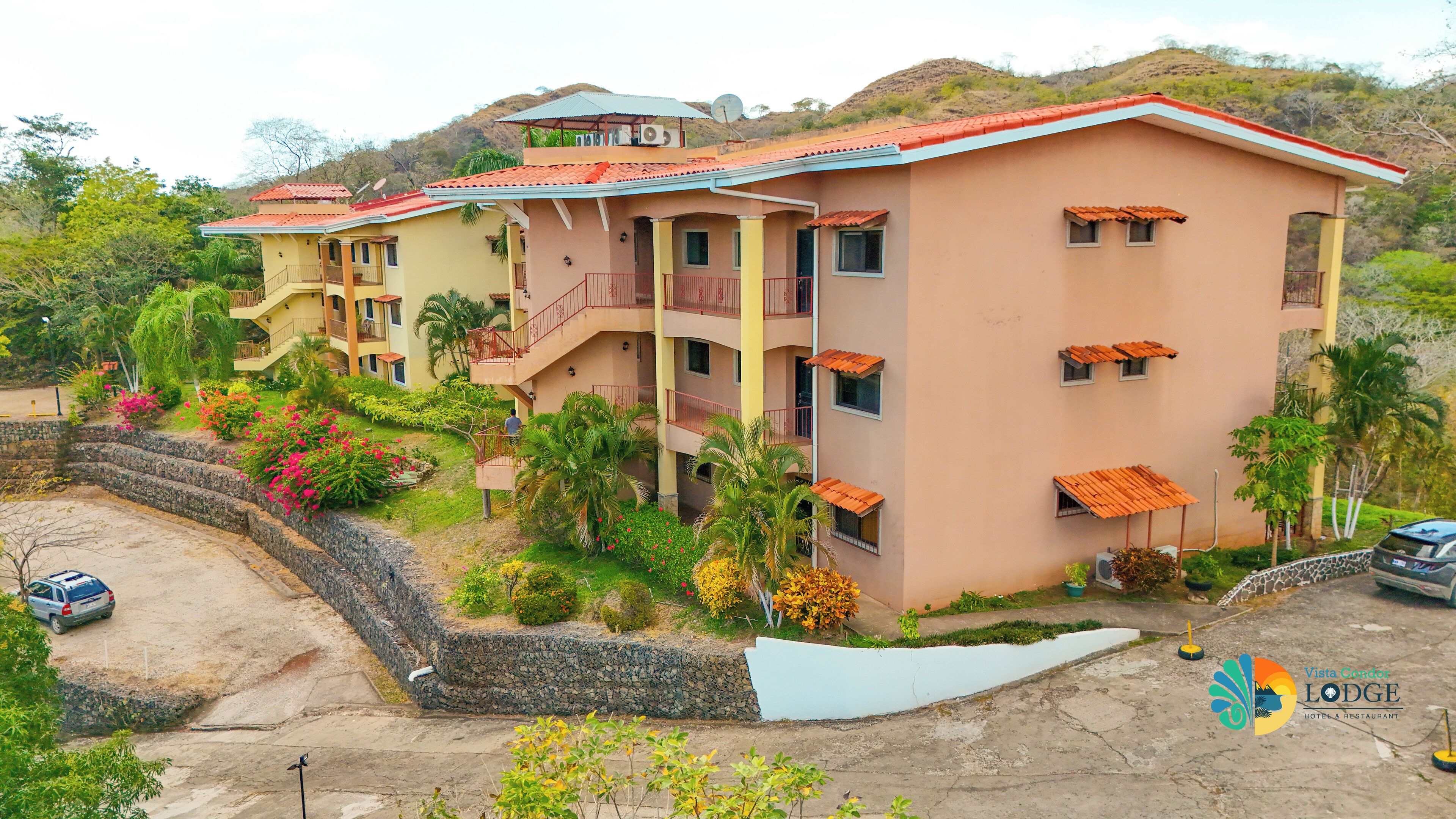 A multi-story hotel with balconies, a parking area, and a landscaped garden.