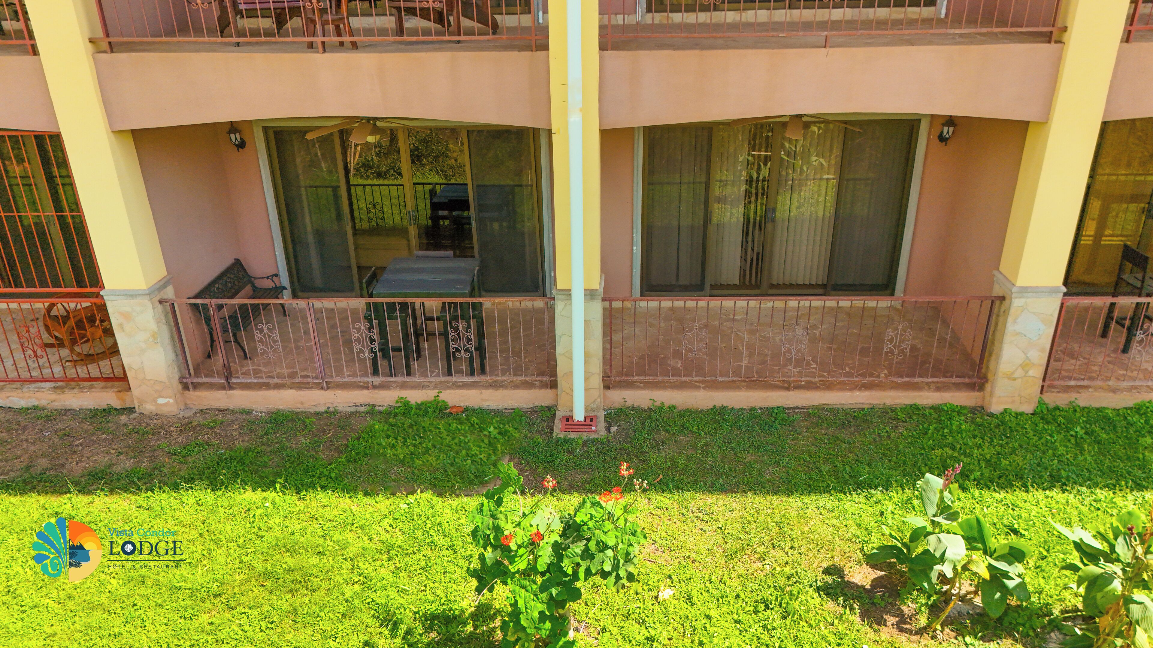 A two-story building with balconies, large windows, and a grassy area in front.