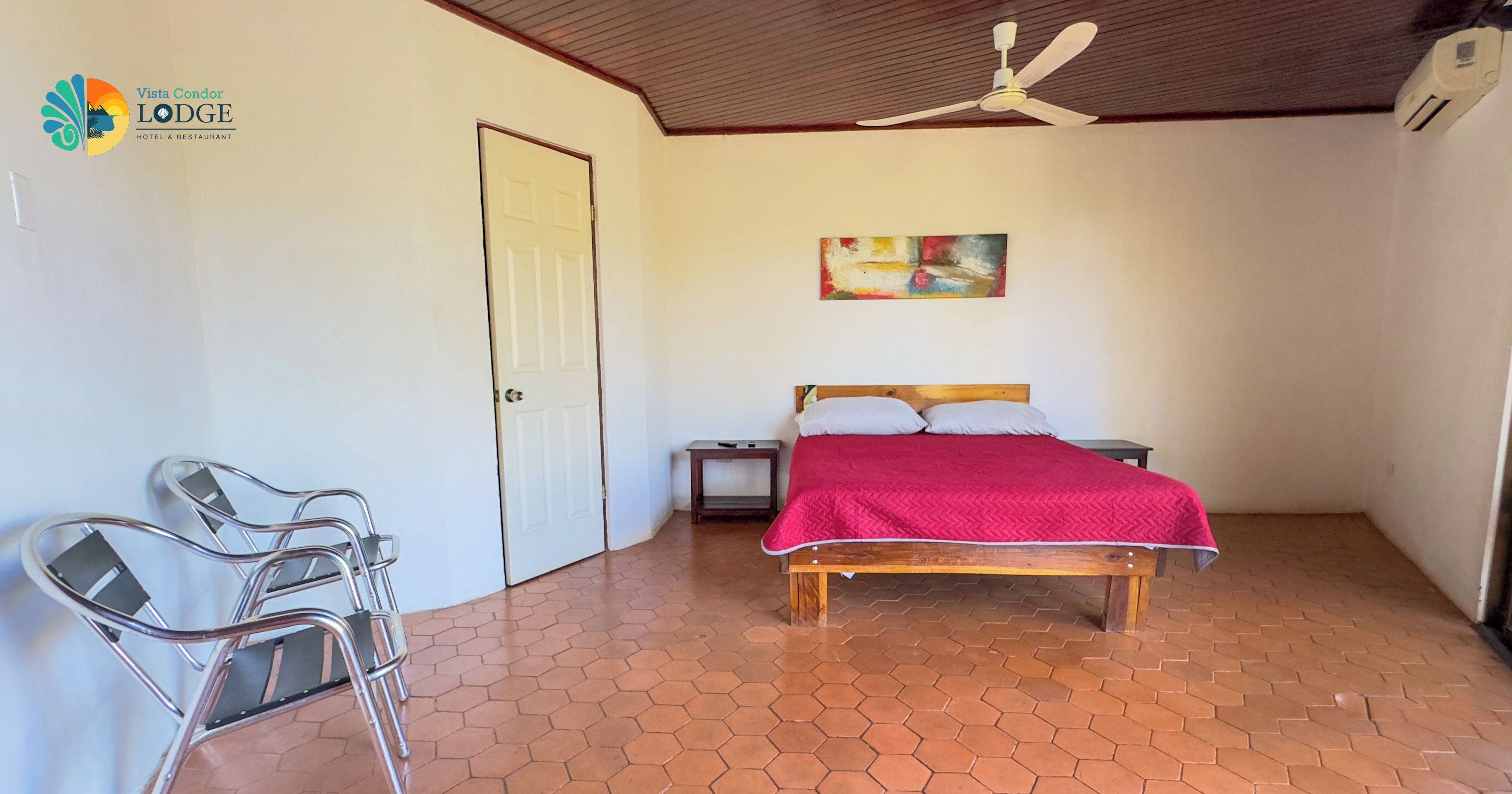 Une chambre d’hôtel avec un lit, un ventilateur de plafond, un tableau au mur et un sol carrelé.