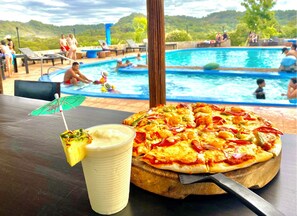 A poolside view with a pizza and a drink on a table. - Vista Condor Lodge (Cabo Velas)