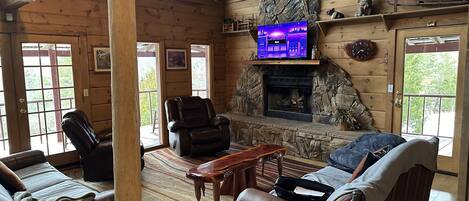 L’intérieur chaleureux d’un chalet avec une cheminée en pierre, des fauteuils en cuir et un téléviseur fixé au-dessus de la cheminée.