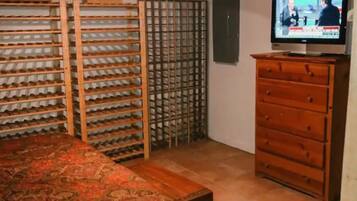 Ein Zimmer mit Deckenventilator, Fernseher auf einer hölzernen Kommode, einem gemusterten Teppich und einem Wandregal mit Schuhen.