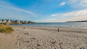 A sandy beach with footprints, a wooden post, and houses in the background.