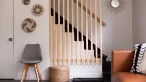 Un interior moderno con un muro de listones de madera, un sillón gris, un otomán tejido y un sofá de cuero marrón.
